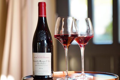 A bottle of Chambolle-Musigny next to two long-stemmed wine glasses filled with red wine.