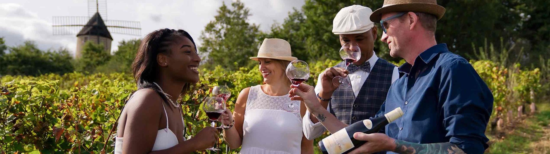 An interracial group of four adults smelling and tasting red wine in a vineyard