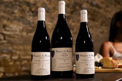Three bottles of Hospices de Beaune wine on a table in front of cheese board.