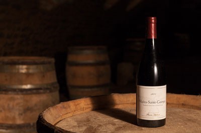 A bottle of Nuits-St-Georges wine sitting atop a barrel.