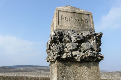 Decorative stone sign that says Pommard in front of a vast sky in Burgundy, France.